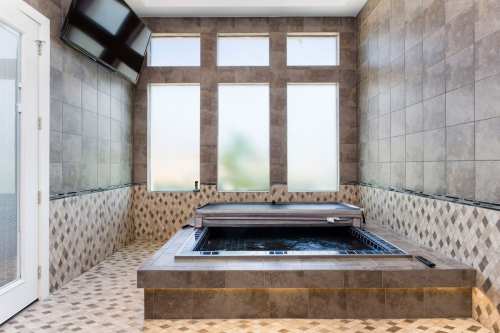 A modern spa room featuring a hot tub, tiled walls, and large windows with frosted glass.