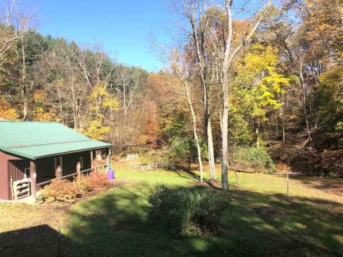 A serene landscape featuring a cabin surrounded by colorful autumn trees and a clear blue sky.