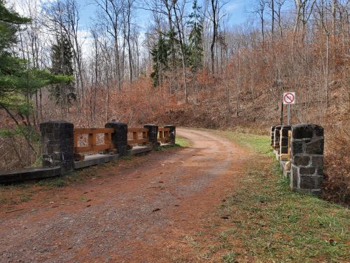 A gravel path leads to a stone bridge surrounded by bare trees and a no trespassing sign.