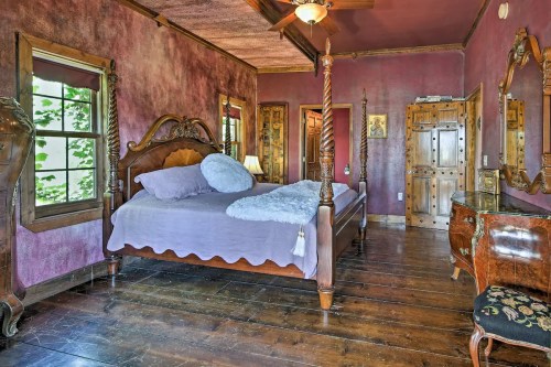 Cozy bedroom with a four-poster bed, purple walls, wooden furniture, and a warm, inviting atmosphere.