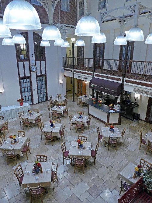 A spacious dining area with round tables, colorful flower centerpieces, and large pendant lights hanging from the ceiling.