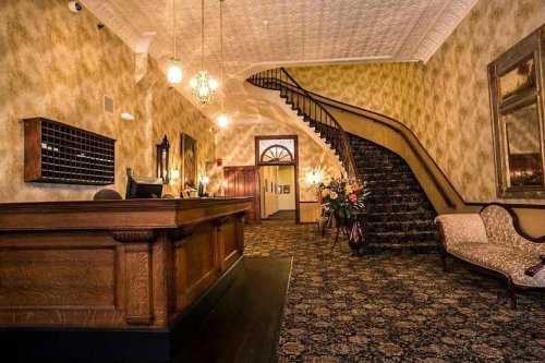 Elegant hotel lobby featuring a wooden reception desk, ornate wallpaper, and a grand staircase.