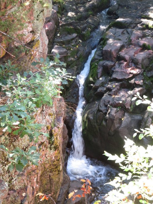 A small waterfall cascades between rocky cliffs, surrounded by lush green foliage.