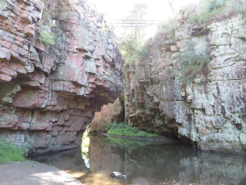 A serene landscape featuring rocky cliffs surrounding a calm waterway, with lush greenery and sunlight filtering through.