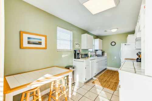 Bright kitchen with green walls, white cabinets, a small table, and modern appliances. Natural light from a window.