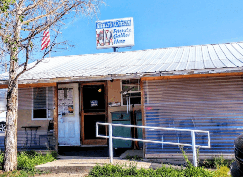 A small diner with a metal roof, sign reading "Friends Diner," and a tree in front under a clear blue sky.