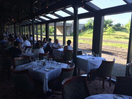 A restaurant interior with tables set for dining, large windows overlooking a green landscape and train tracks.