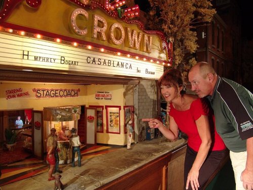 A woman and a man admire a detailed miniature theater display featuring classic films and characters.