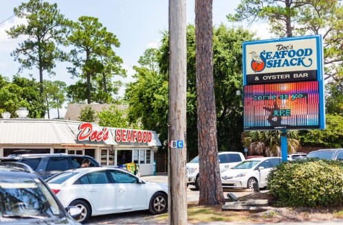Exterior of Doc's Seafood Shack & Oyster Bar, featuring a sign and parked cars under a sunny sky.