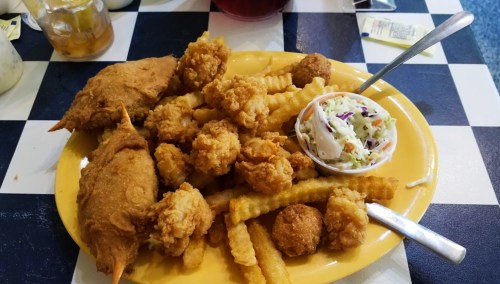 A yellow plate filled with fried shrimp, crinkle-cut fries, coleslaw, and two pieces of fried fish.