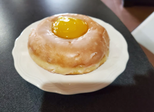 A glazed donut with a bright yellow icing in the center, placed on a small white plate.