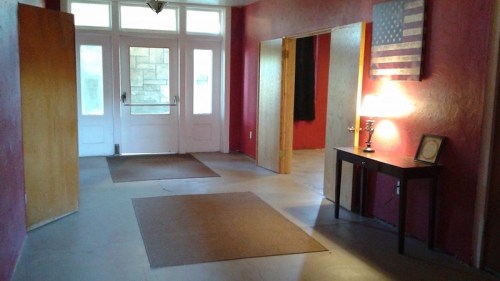 A spacious entryway with red walls, two doors, a lamp on a table, and an American flag on the wall.