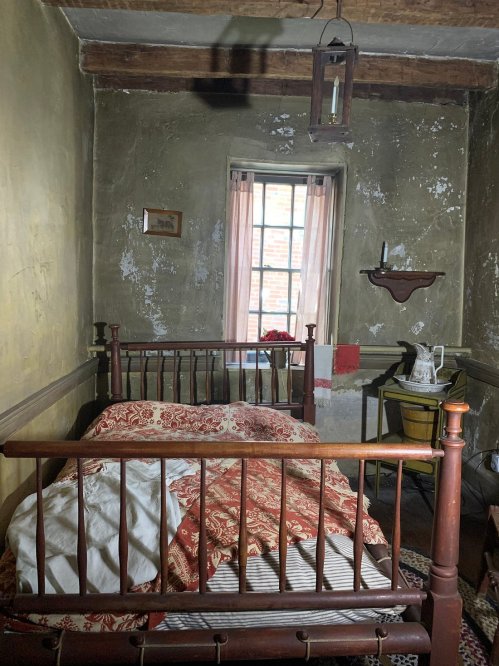 A rustic bedroom with a wooden bed, vintage decor, and a window letting in natural light.