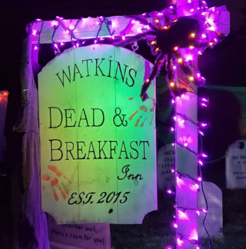 A spooky sign for "Watkins Dead & Breakfast Inn" adorned with colorful lights and a spider, set in a Halloween theme.
