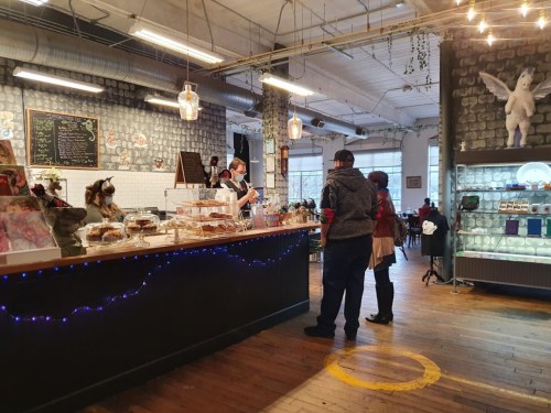A cozy café interior with a counter displaying baked goods, patrons interacting, and warm lighting.