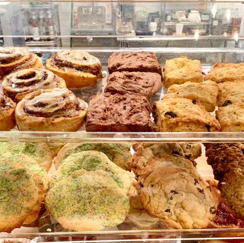 A display case filled with various baked goods, including cinnamon rolls, brownies, scones, and cookies.