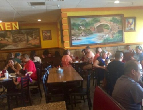 A busy restaurant interior with diners at tables, colorful murals on the walls, and a warm, inviting atmosphere.
