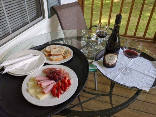 A table set with a charcuterie platter, wine glasses, and a bottle of red wine on a patio.