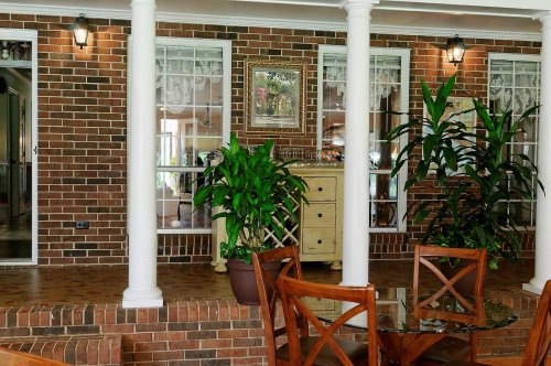 A cozy indoor space with brick walls, plants, and wooden furniture, featuring columns and decorative lighting.
