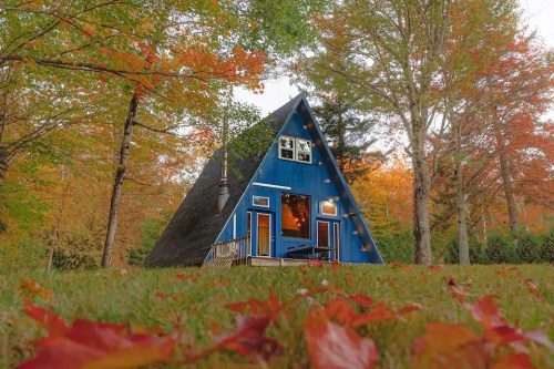 A blue A-frame cabin surrounded by colorful autumn foliage and fallen leaves.