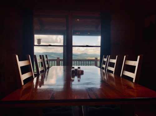 A wooden dining table with chairs, overlooking a scenic mountain view through large windows.