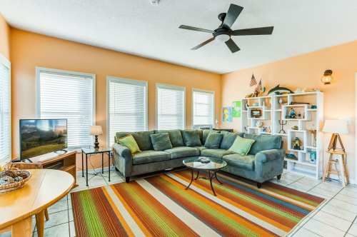 Cozy living room with a green sectional sofa, coffee table, TV, and colorful rug, featuring bright orange walls and natural light.