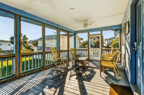 A sunny screened porch with wooden furniture and a view of nearby houses and greenery.