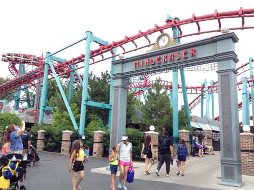 Entrance to a roller coaster named "Minderaser" with people walking by and a red track in the background.