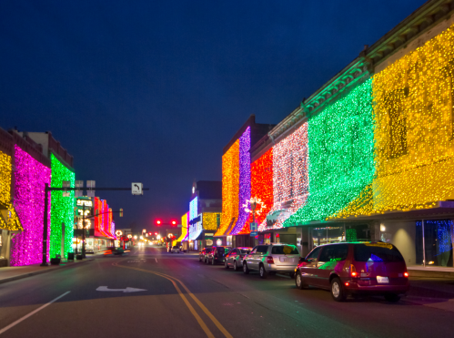 Colorful holiday lights adorn buildings along a street at night, creating a festive atmosphere.