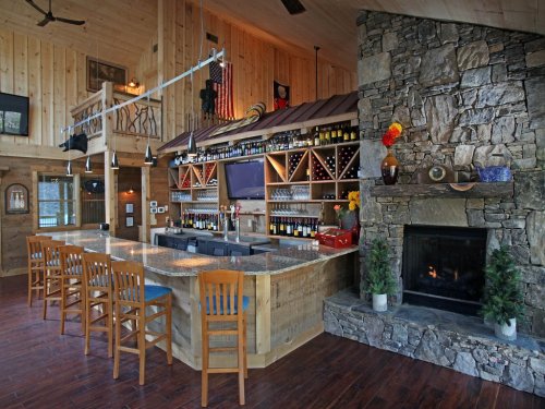 A cozy wooden bar area with a stone fireplace, shelves of wine, and seating at a curved counter.