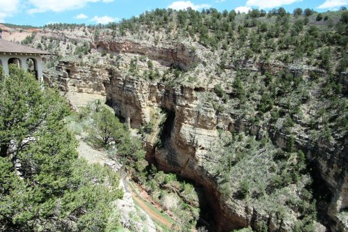 A scenic view of a canyon surrounded by greenery and rocky cliffs under a blue sky with scattered clouds.