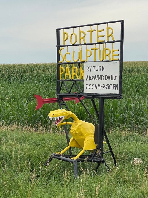 A colorful sign for Porter Sculpture Park featuring a yellow dinosaur sculpture and information about RV turnarounds.