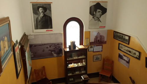 A staircase with historical photos and artifacts displayed on the walls, leading to a window with natural light.