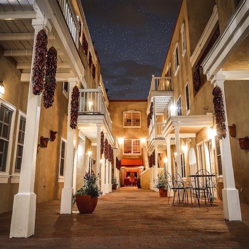A charming courtyard at night, featuring starry skies, hanging chili peppers, and cozy seating arrangements.