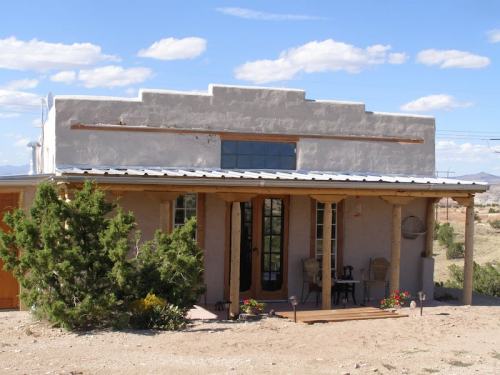 A small adobe-style house with a porch, surrounded by desert landscape and blue skies.