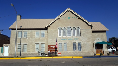 Historic building with a stone facade, featuring large windows and an American flag, housing the Herkimer Memorial Museum.
