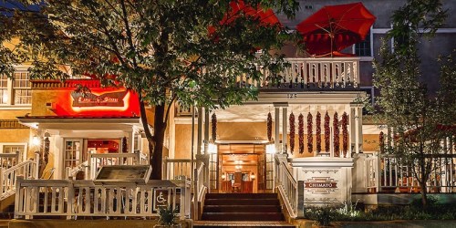 A charming restaurant exterior with red umbrellas, warm lighting, and decorative plants at night.