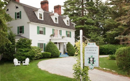 A charming white house with green shutters, surrounded by trees, featuring a sign for "Hampton Terrace" in front.