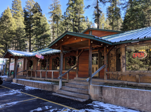 A rustic wooden building with a metal roof, surrounded by trees, featuring "open" signage and holiday decorations.