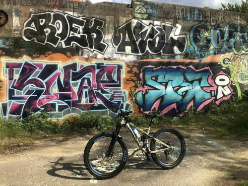 A mountain bike parked in front of a colorful graffiti wall with various artistic designs and vibrant colors.