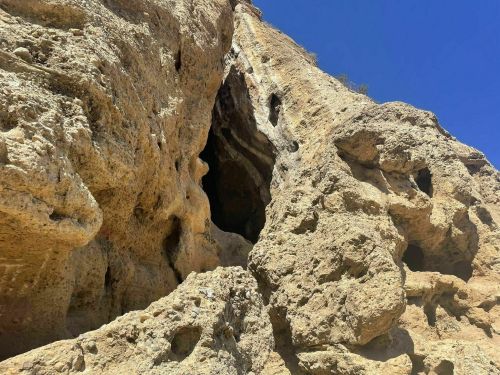 A rugged rock formation with a cave entrance, set against a clear blue sky.