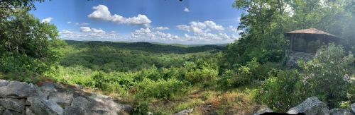Panoramic view of lush green hills under a blue sky with fluffy clouds, featuring a gazebo in the foreground.