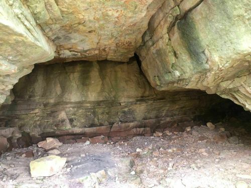 A rocky cave entrance with layered stone walls and scattered debris on the ground.