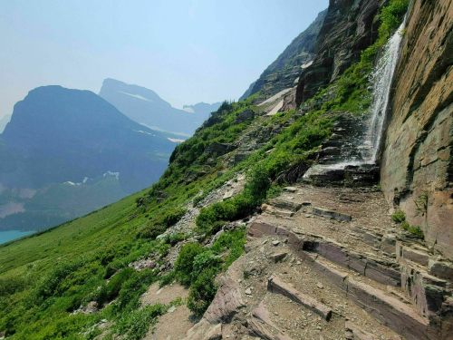 A scenic mountain landscape featuring a waterfall cascading down rocky terrain, surrounded by lush greenery and distant peaks.