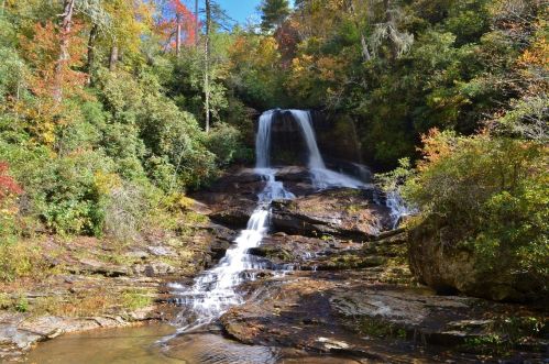 A serene waterfall cascades over rocks, surrounded by vibrant autumn foliage and lush greenery.