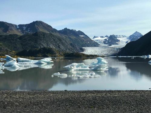 A serene landscape featuring a calm lake with icebergs, surrounded by mountains and a glacier in the background.