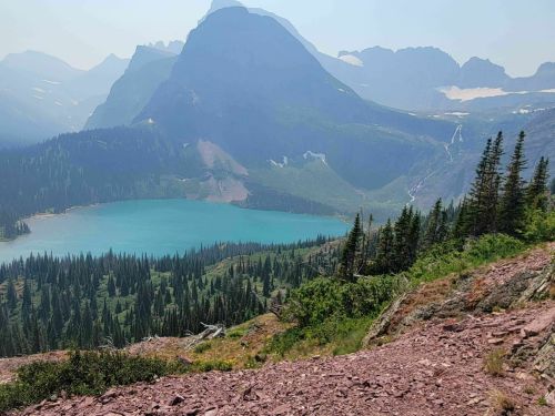 A scenic view of a turquoise lake surrounded by mountains and dense forests under a clear blue sky.