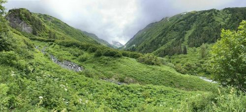 A lush green valley surrounded by mountains under a cloudy sky, with a stream flowing through the landscape.