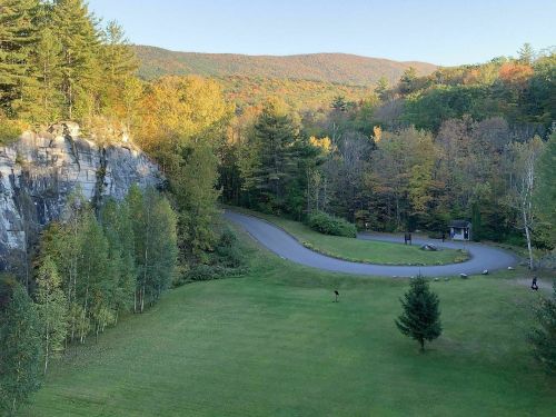 A scenic view of a winding road through colorful autumn trees and a rocky cliff in the background.