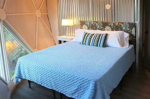 Cozy bedroom with a blue blanket, floral headboard, and a bedside lamp, featuring a unique geometric wall design.